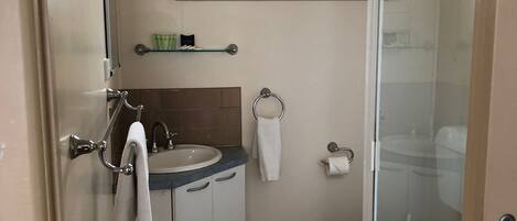 A bathroom with a sink, mirror, towel rack, toilet, and a shower area.