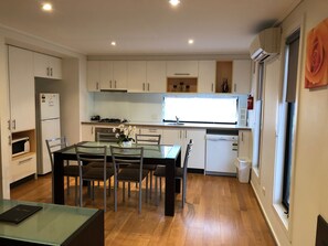 A compact kitchen with white cabinets, a dining table with chairs, a microwave, a refrigerator, and a window with a view. - Koonwarra Holiday Park (Lakes Entrance)