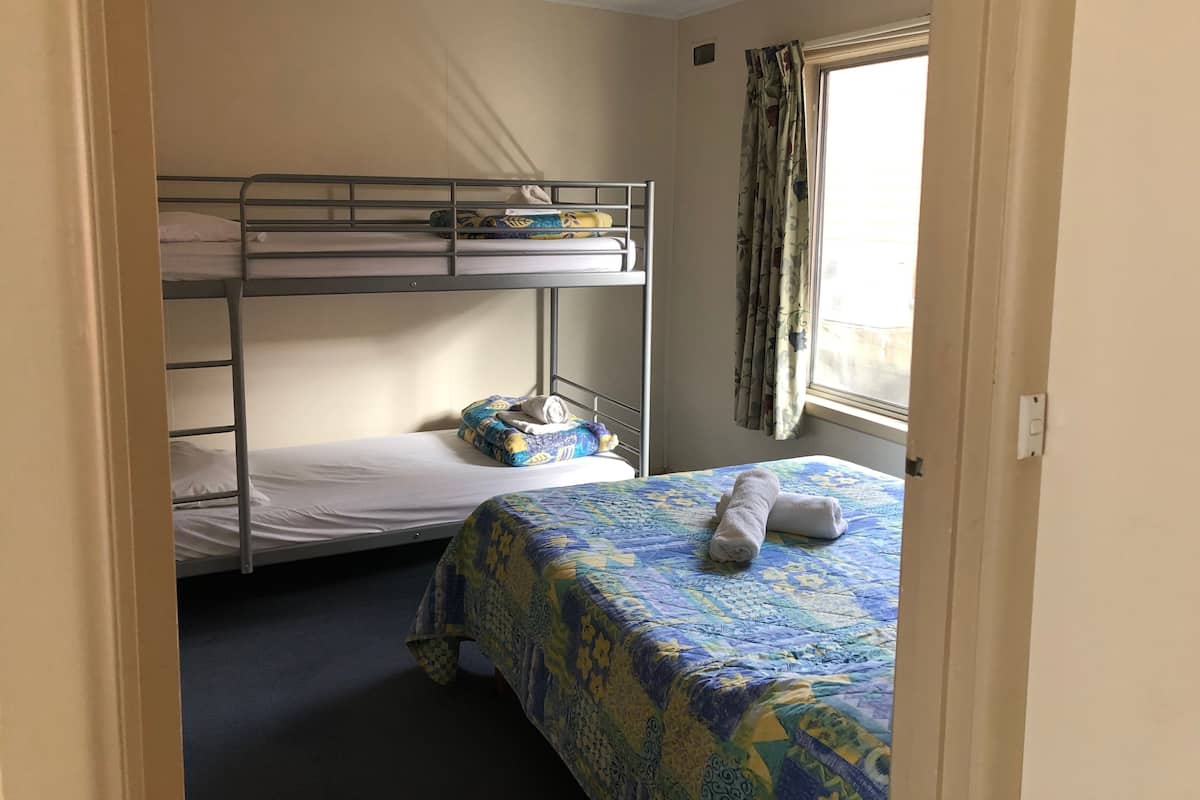 Une chambre de dortoir avec des lits superposés, un lit simple et une fenêtre avec des rideaux.
