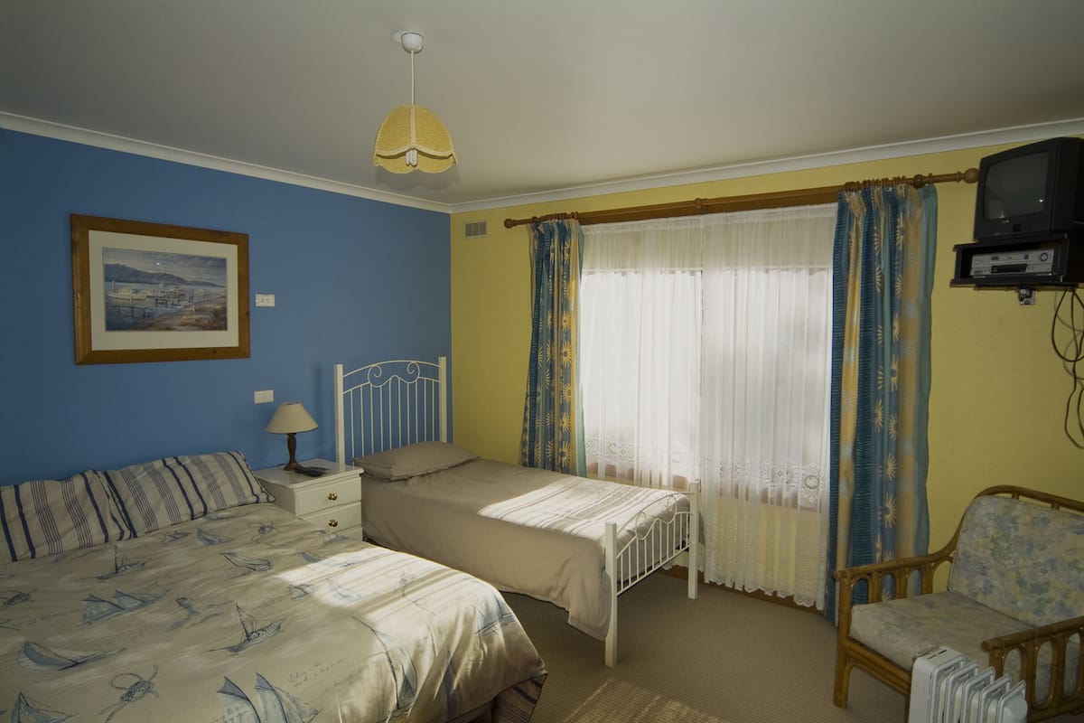 Une chambre avec deux lits, une chaise, un téléviseur et une fenêtre avec des rideaux.