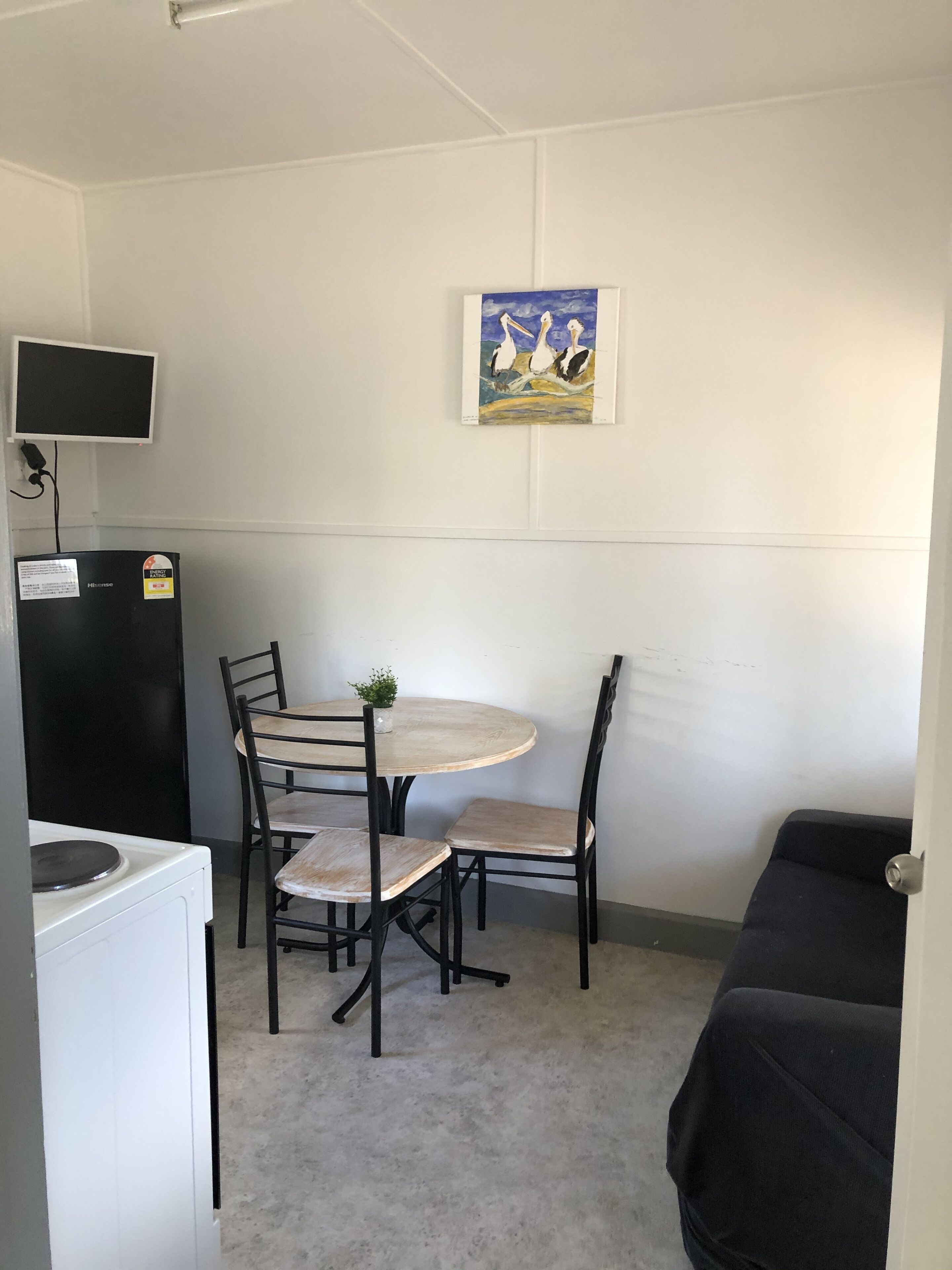 A small, compact room with a kitchenette, a dining table with four chairs, and a single bed.