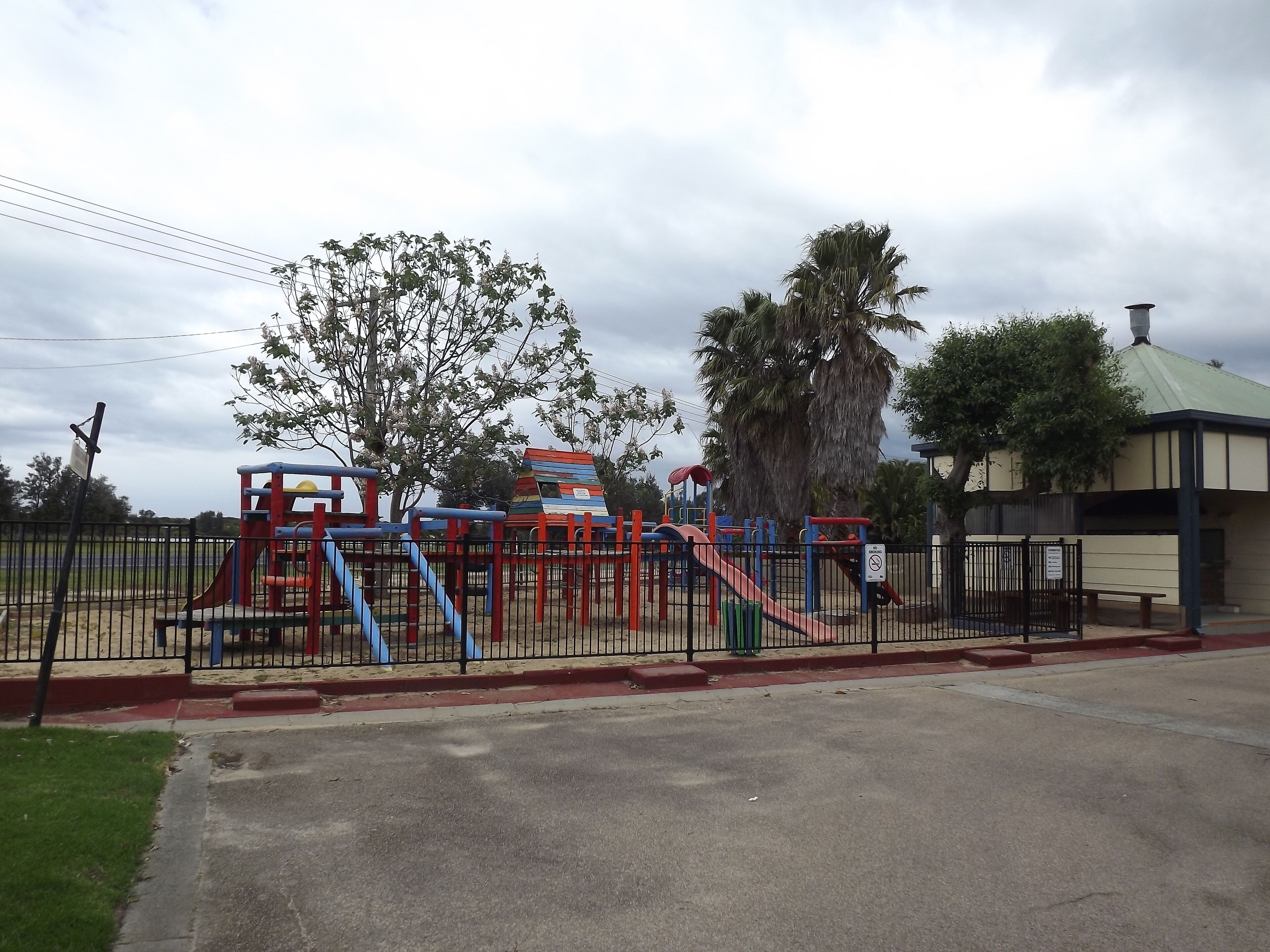Un parque infantil con diversas estructuras de juego, un área cercada y un edificio con techo verde.