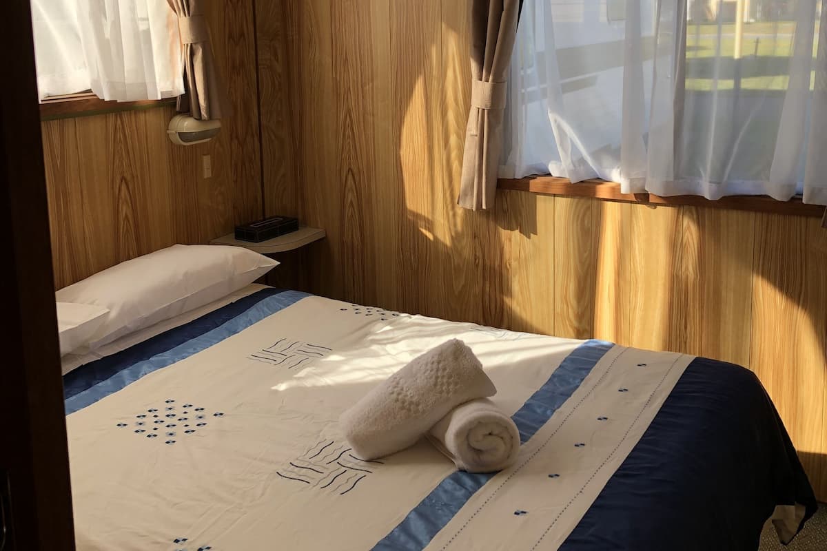 Une pièce aux murs recouverts de lambris en bois, un lit avec une couvre-lit à rayures bleues et blanches, et une fenêtre avec des rideaux.