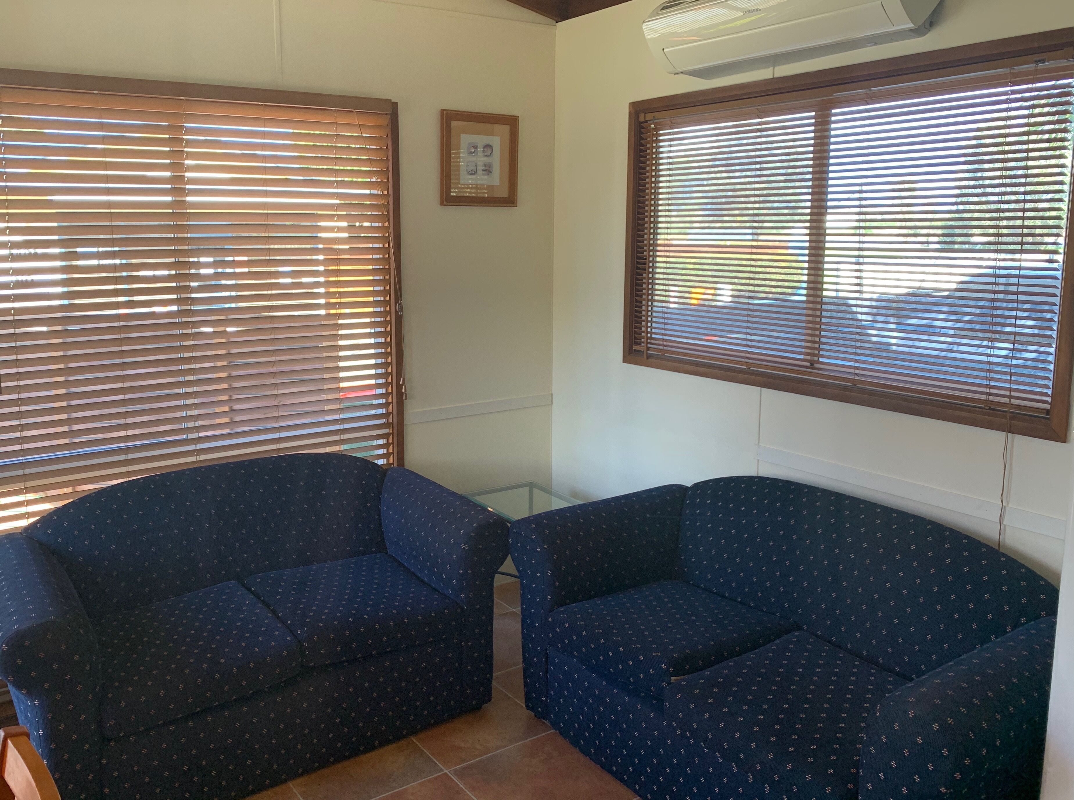 A room with two blue patterned sofas, a ceiling fan, and a framed picture on the wall.