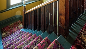 A staircase with a wooden handrail, a chandelier, and a window with a view. - Healesville Hotel (Healesville)