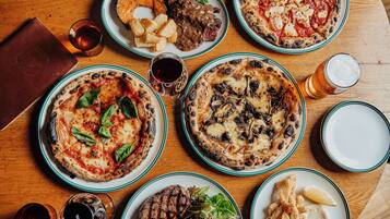 Diversos platos, incluyendo pizzas, ensaladas y carnes a la parrilla, dispuestos sobre una mesa de madera.