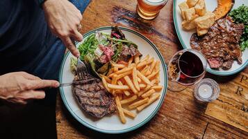Een eettafel met een bord steak, friet en salade, een glas bier en een kaars.