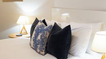 A neatly made bed with white linens and a variety of pillows, including a blue patterned one.