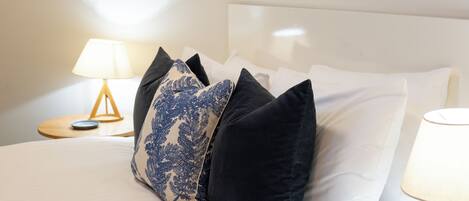 A neatly made bed with white linens and a variety of pillows, including a blue patterned one.