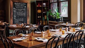 A restaurant with a wooden table and chairs, a chalkboard menu, and a view of the outdoors through large windows.