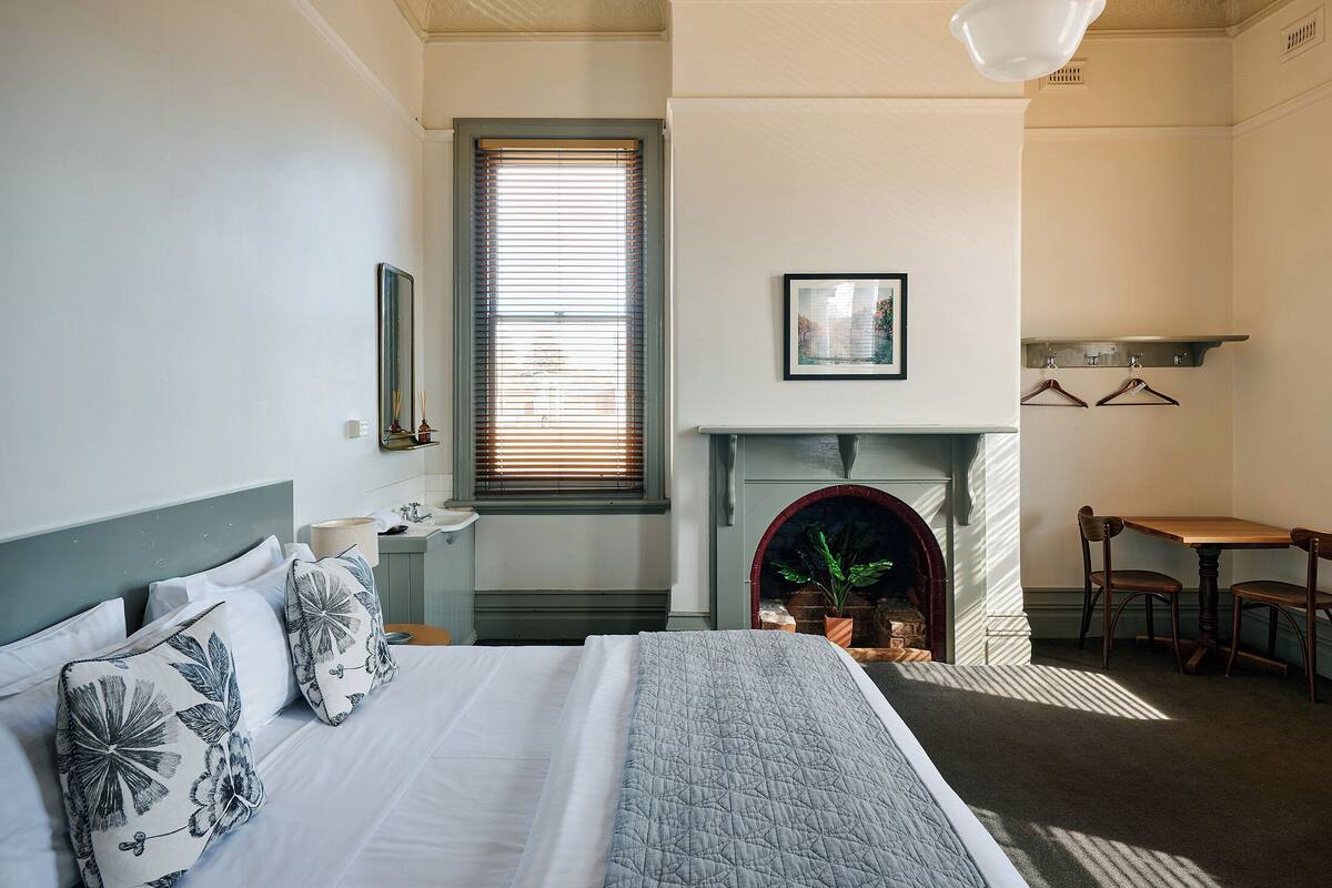 A bedroom with a bed, a fireplace, a dining table, and a window with blinds.