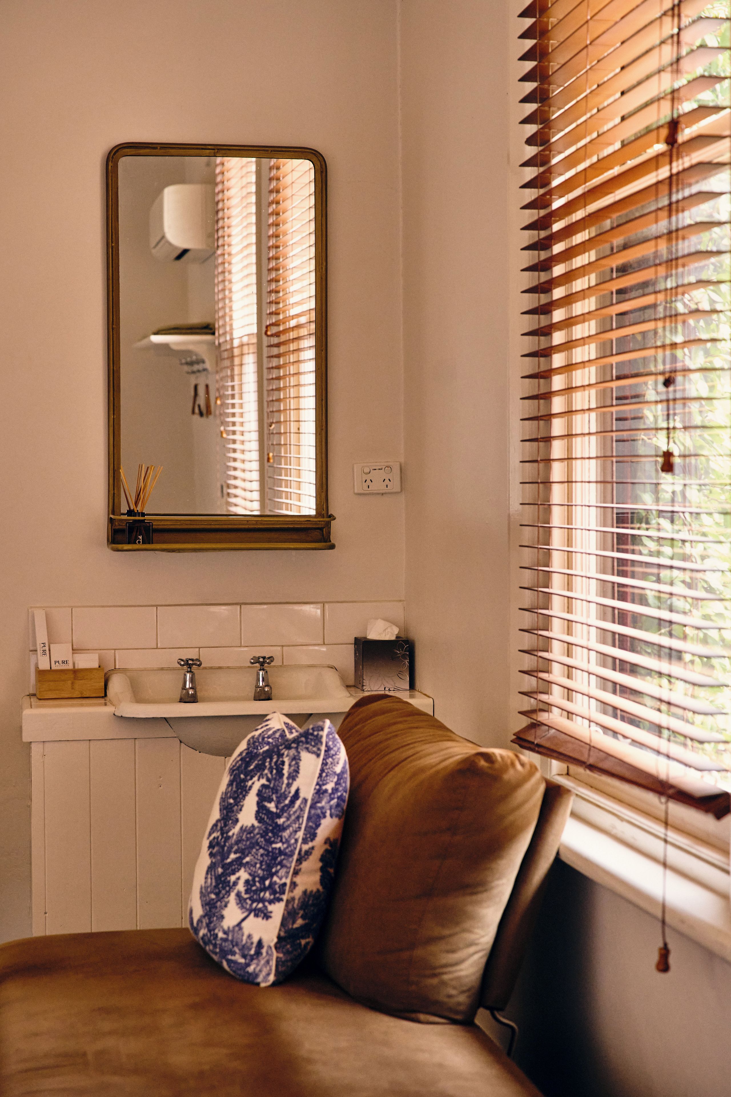 A bathroom with a mirror, sink, and window with blinds.