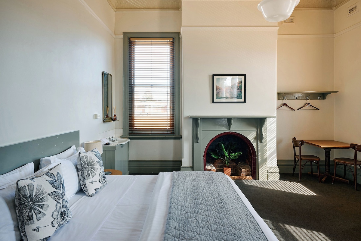 A bedroom with a bed, a fireplace, a dining table, and a window with blinds.