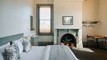 Un dormitorio con cama, chimenea, ventana con persianas, espejo y un cuadro en la pared.