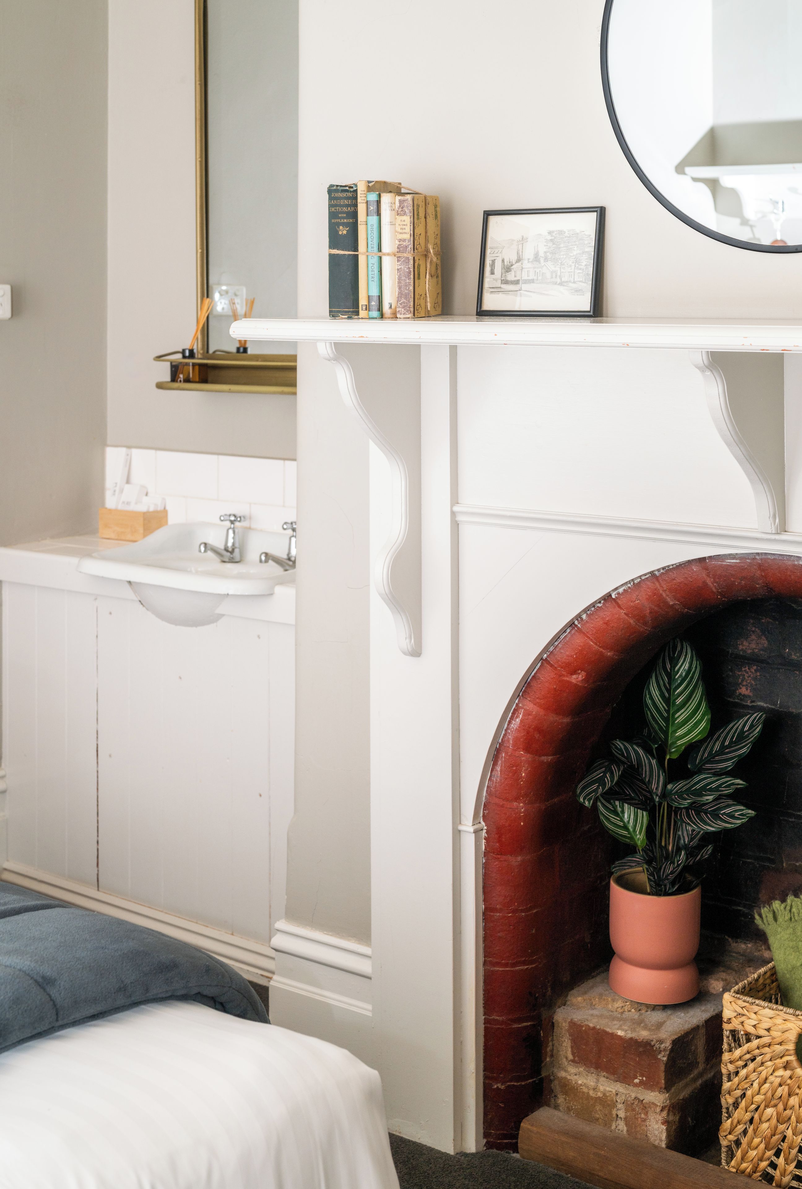 Une pièce avec une cheminée blanche, un lit, un lavabo et un miroir.