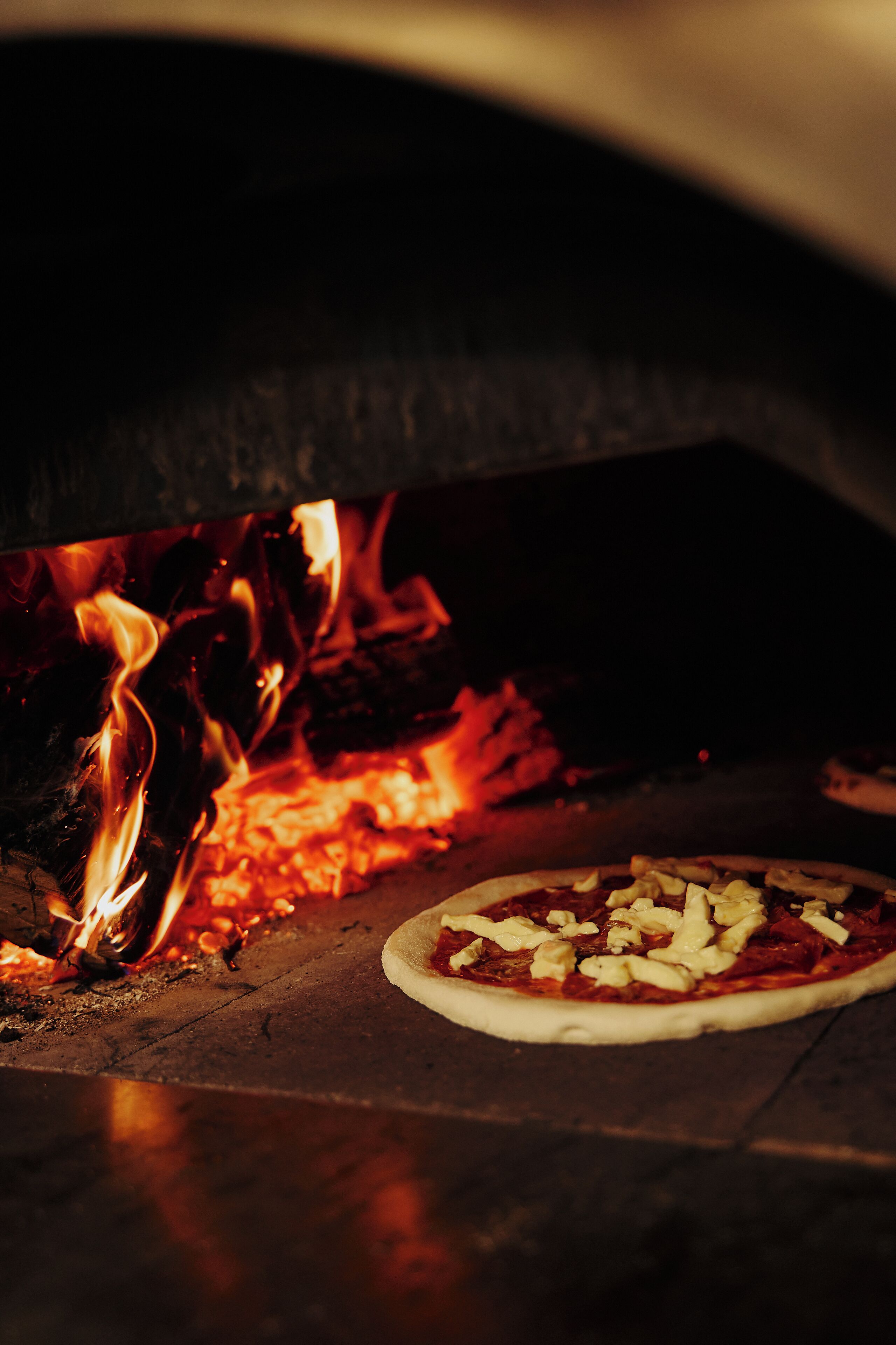 Pizza dentro de un horno de leña con llamas a la vista.
