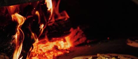 A pizza inside a wood-fired oven with flames visible.