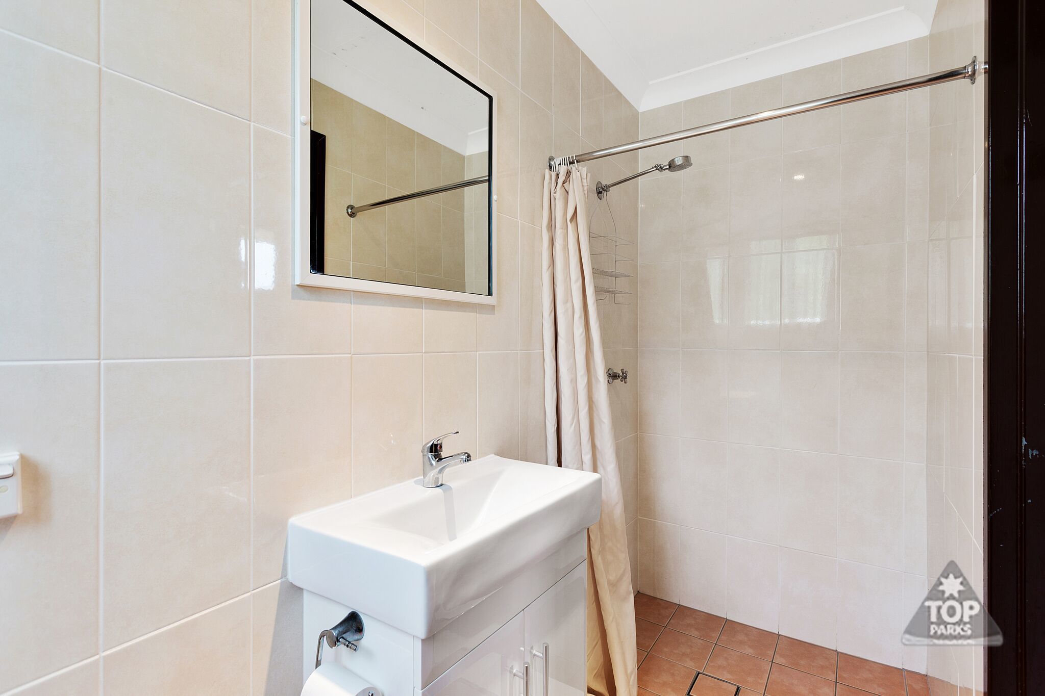 Une salle de bain avec un lavabo blanc, un miroir et une douche avec un rideau.