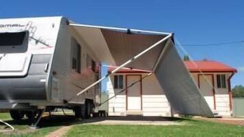A caravan with a large awning, a red roof, and a white exterior.