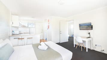 A hotel room with a bed, a desk, a chair, a TV, and a kitchenette.