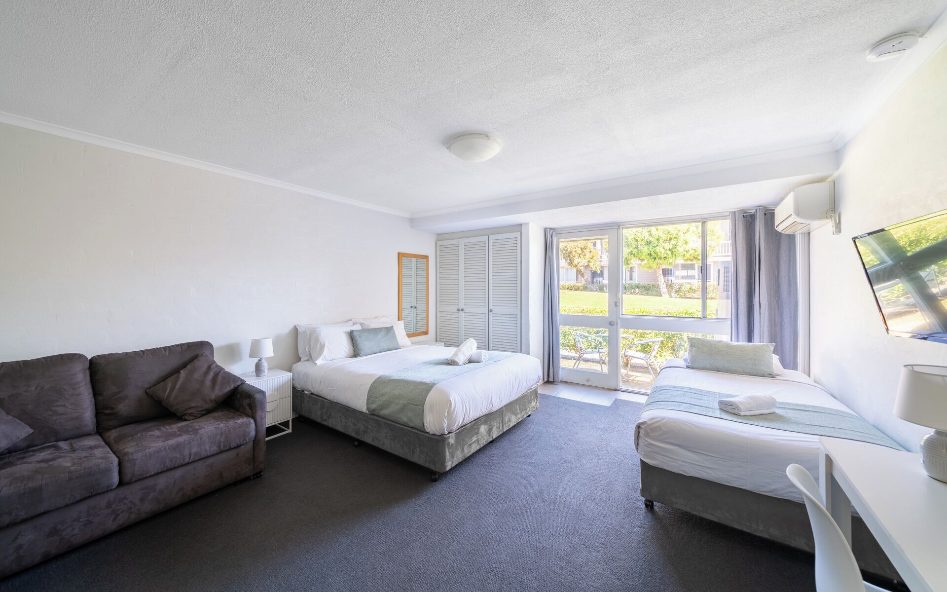 A hotel room with a bed, a sofa, a desk, and a view of the outdoors.