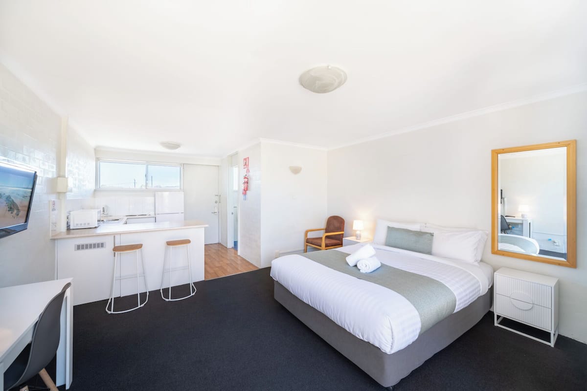 A modern hotel room with a large bed, a desk with a chair, a small table, and a TV.