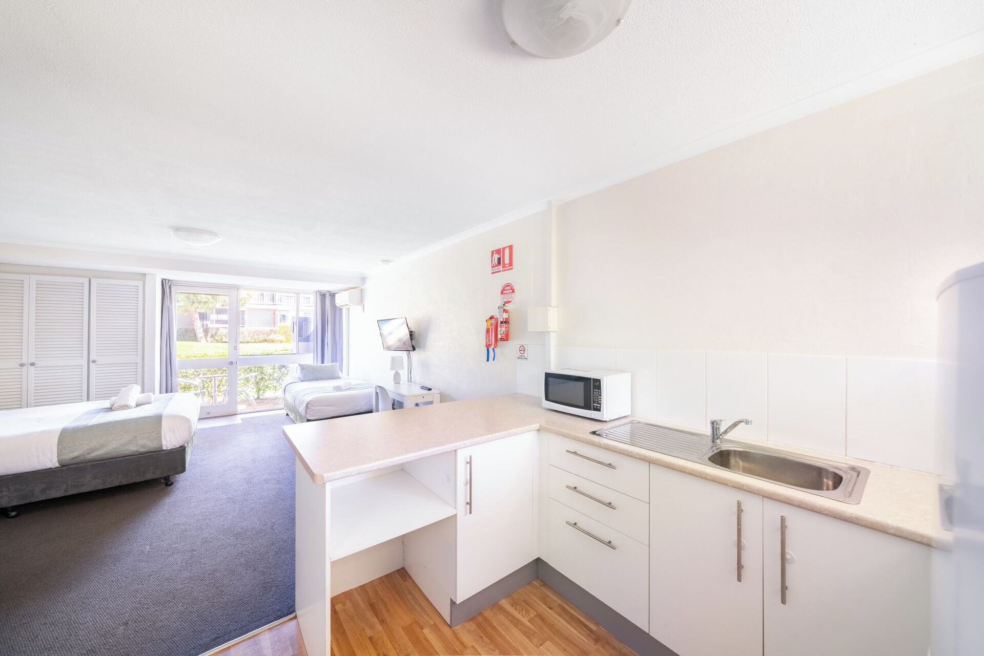 Habitación de hotel moderna y funcional con cama, escritorio, kitchenette pequeña y vista al exterior.