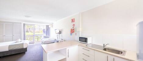 Habitación de hotel moderna y funcional con cama, escritorio, kitchenette pequeña y vista al exterior.