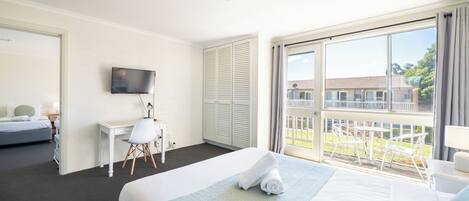 Habitación de hotel con cama, escritorio, silla, televisor y balcón con mobiliario exterior.