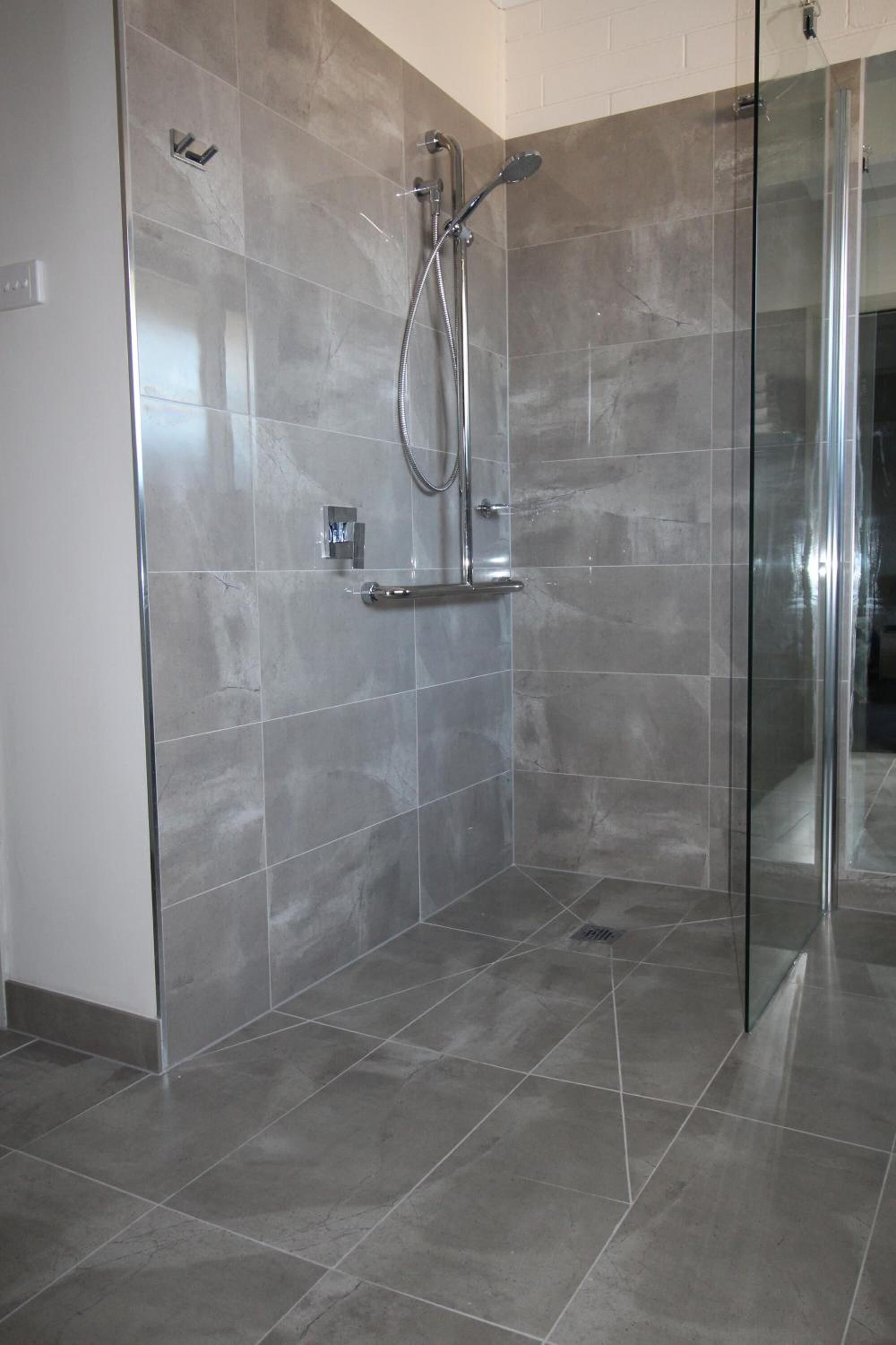 A modern bathroom with a glass-enclosed shower, grey tiles, and a visible hand dryer.