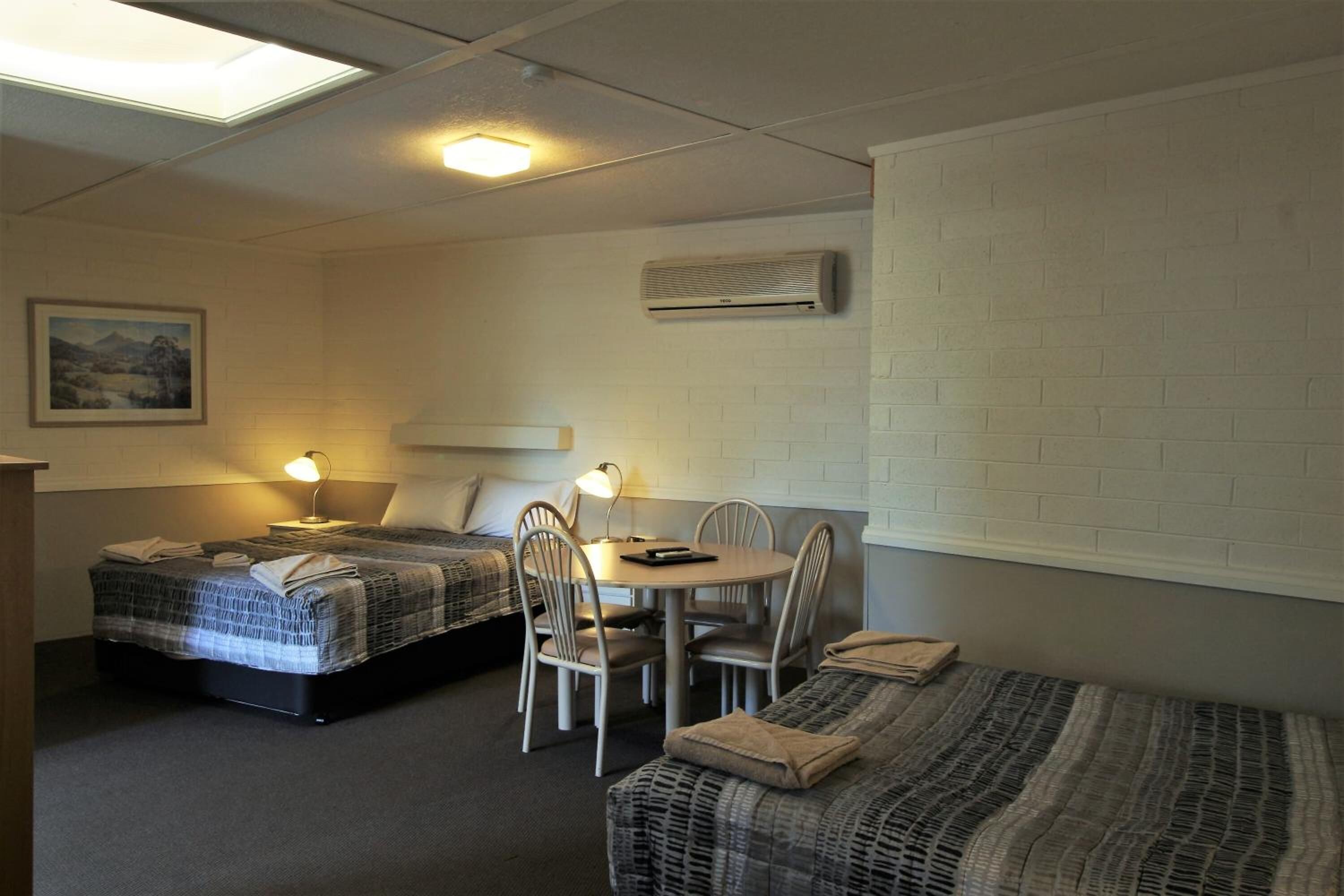 A room with two beds, a dining table with chairs, a ceiling light, and a wall-mounted air conditioner.