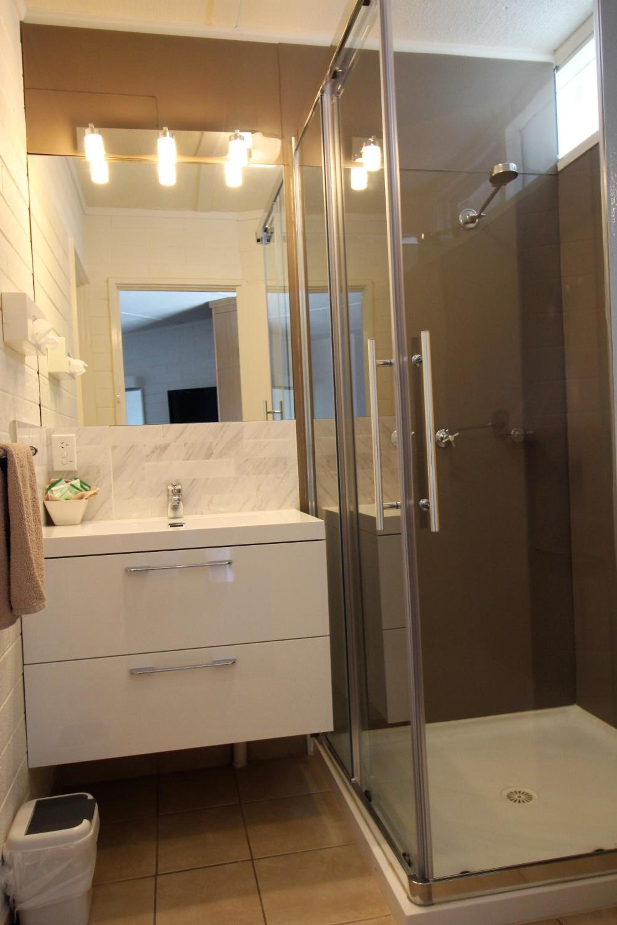 Un bany modern amb dutxa de vidre, un lavabo blanc amb mirall i una tovallola penjada a la paret.