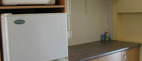 Una cocina con armarios de madera, un refrigerador blanco y un microondas encima.