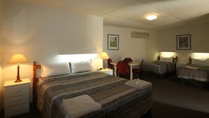 A hotel room with two single beds, a desk, and a chair. There are two bedside tables with lamps and a small table with a chair.