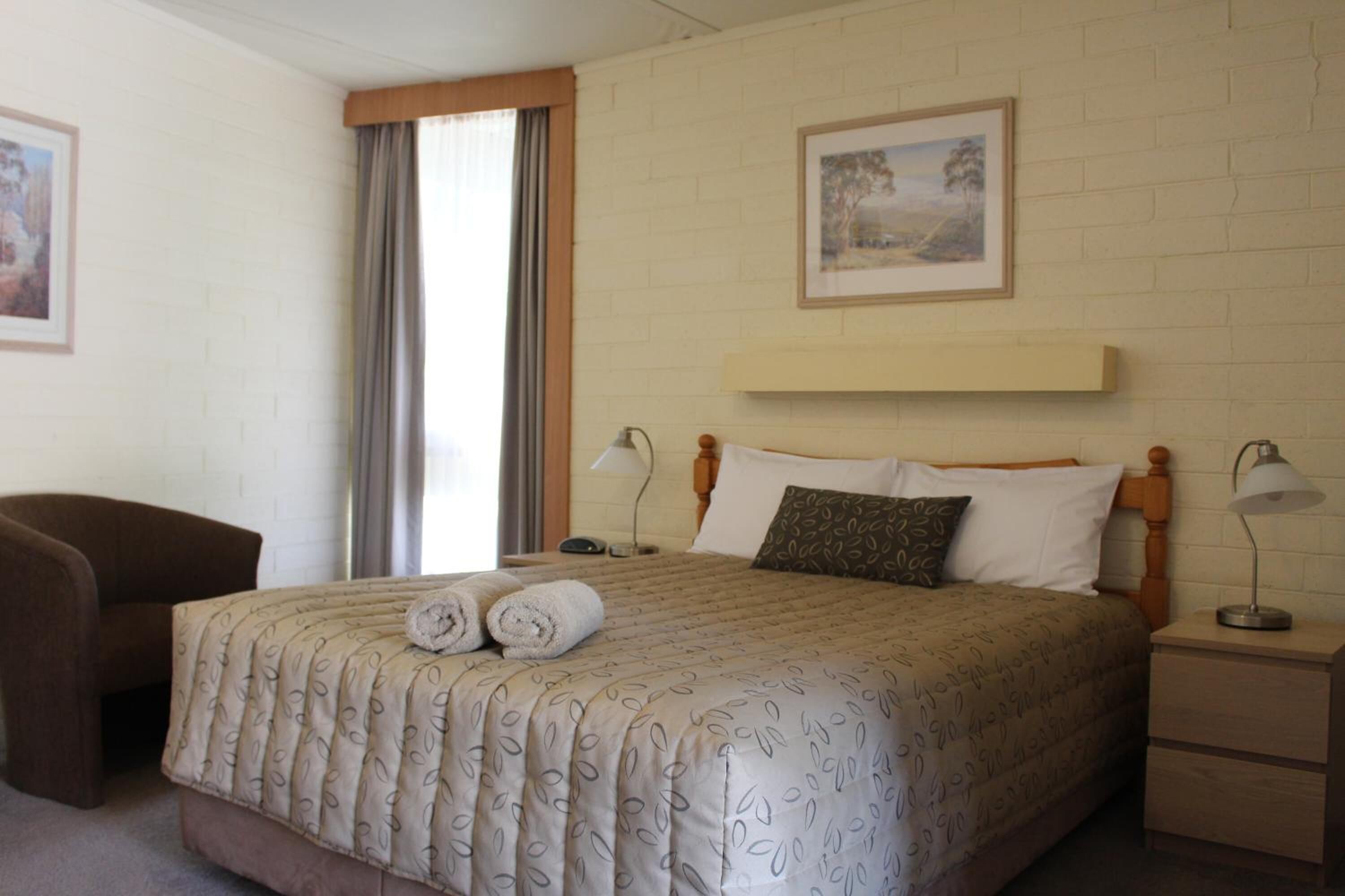 A neatly arranged hotel room with a bed, a chair, a nightstand, and a window with curtains.