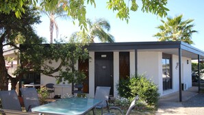 A modern building with a glass table and chairs in the foreground, surrounded by greenery and palm trees.