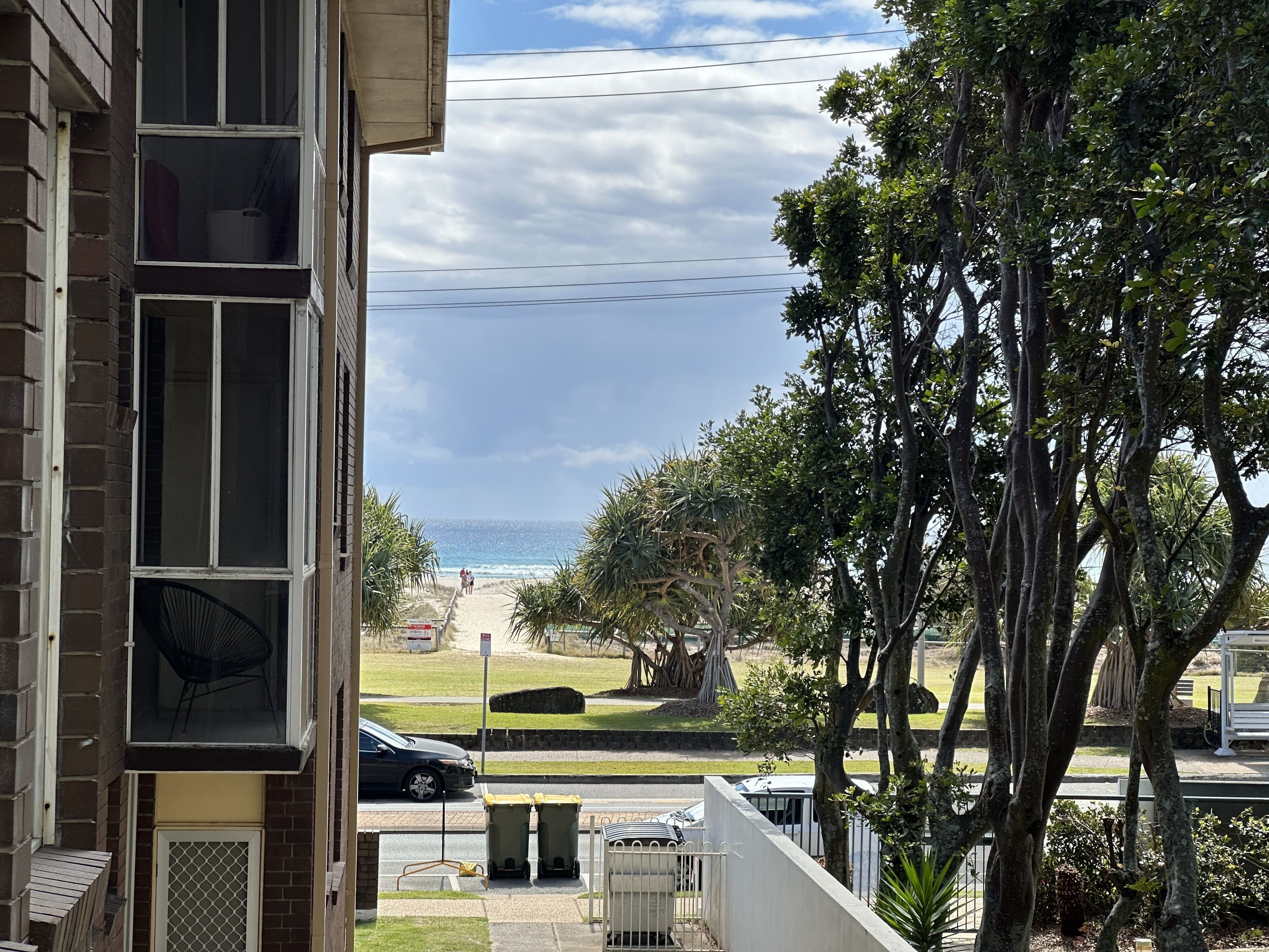 A residential building with a view of the beach, a parked car, and a trash bin.