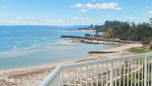 A coastal view with a beach, rocky shoreline, and a distant building. - Meridian Tower (Coolangatta)