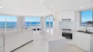 A modern kitchen with a large island, white cabinetry, and a view of the ocean. - Meridian Tower (Coolangatta)