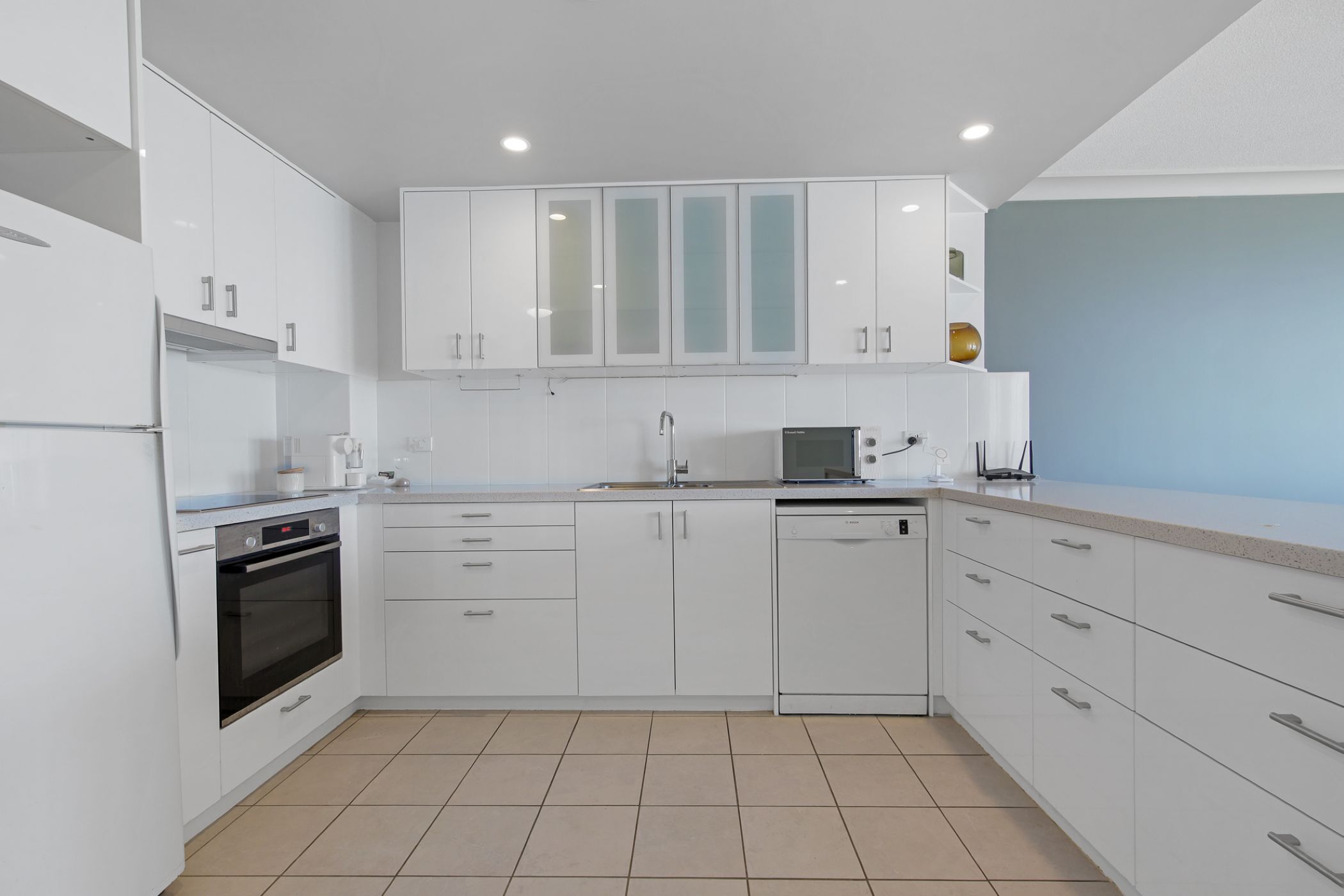 A modern kitchen with white cabinetry, a built-in oven, and a dishwasher.