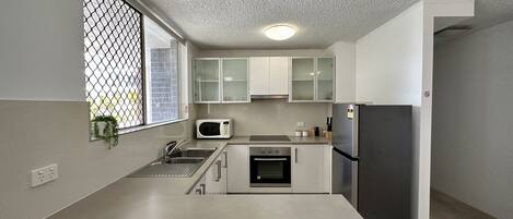 A modern kitchen with a stainless steel refrigerator, a microwave, and a built-in oven. There is a window with a view of the outside, and the kitchen has white cabinets.