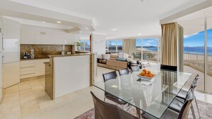 A modern kitchen with white cabinets, a granite countertop, and a dining area with a glass table and chairs. - Meridian Tower (Coolangatta)