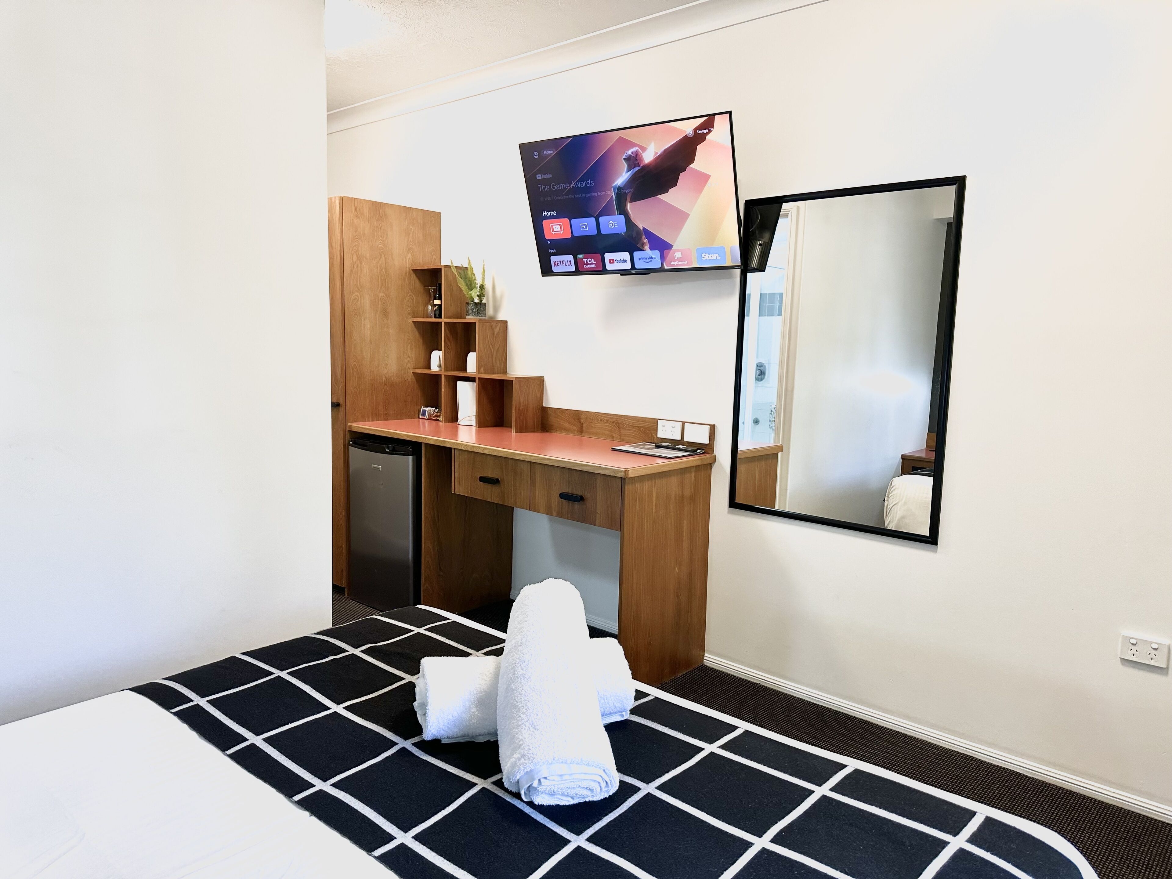A hotel room with a bed, a desk, a television, and a mirror.