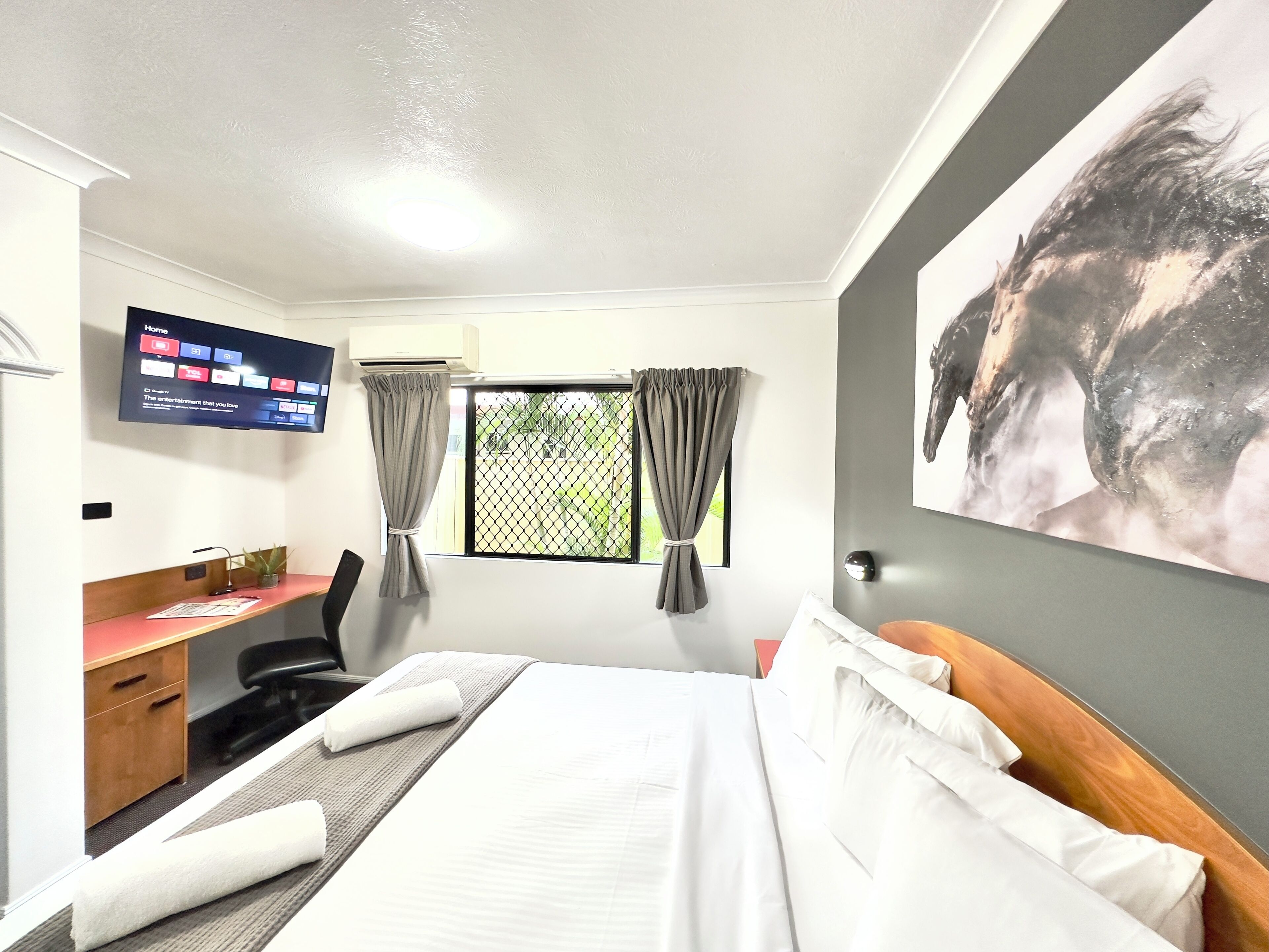 A hotel room with a bed, desk, chair, TV, and a window with curtains.