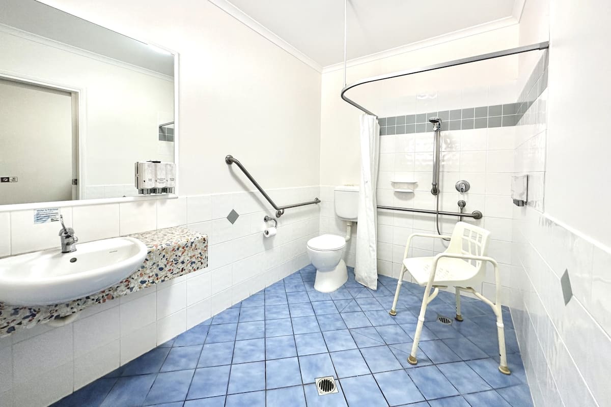 A bathroom with a white sink, toilet, and shower area, including grab bars and a wheelchair-accessible chair.