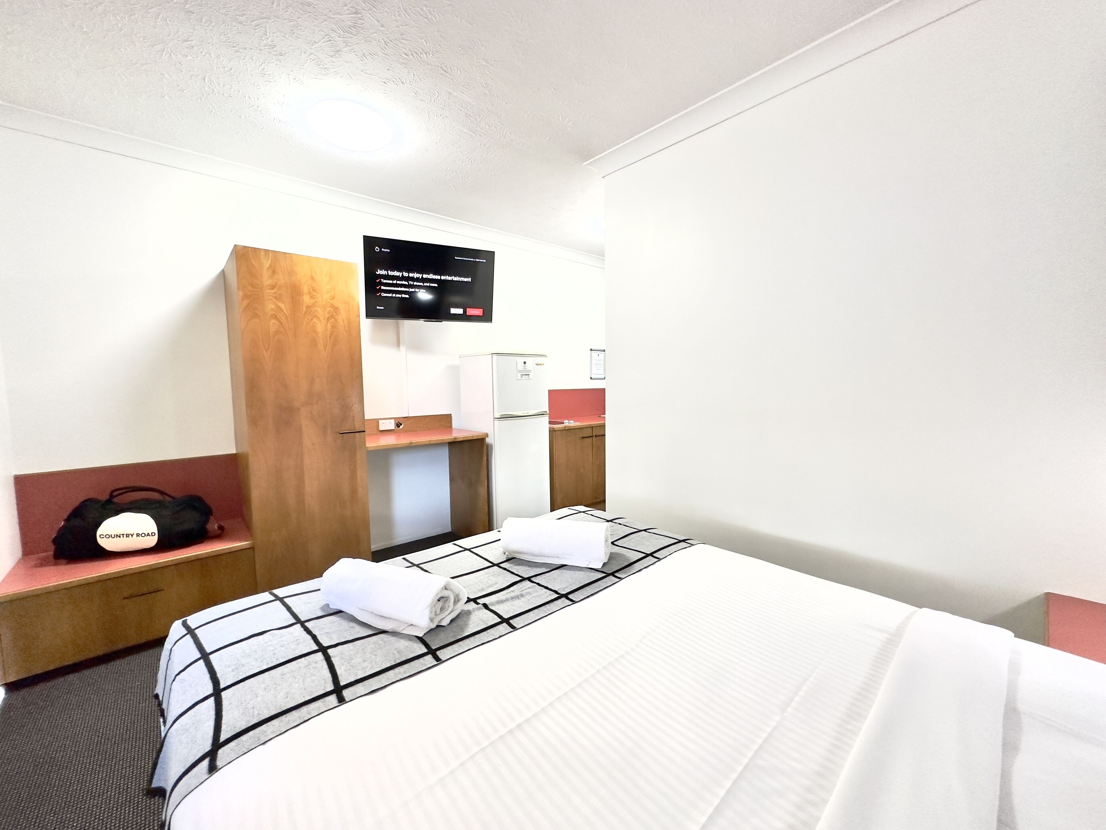 A hotel room with a bed, a desk, a chair, a TV, and a minibar.