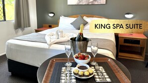 Una suite tipo King Spa con una cama, una mesita de noche con una botella de champán, un bol de fresas y un plato de bombones.