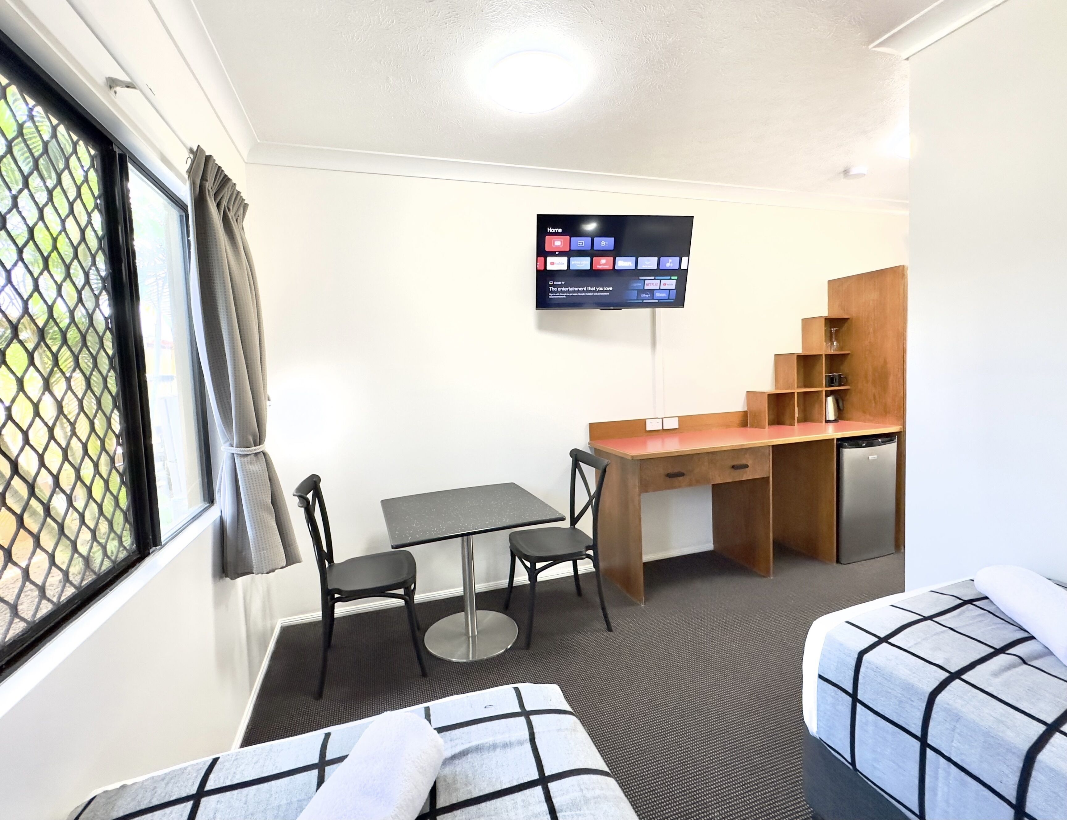 A compact room with a bed, a desk with a chair, a television, and a kitchenette.