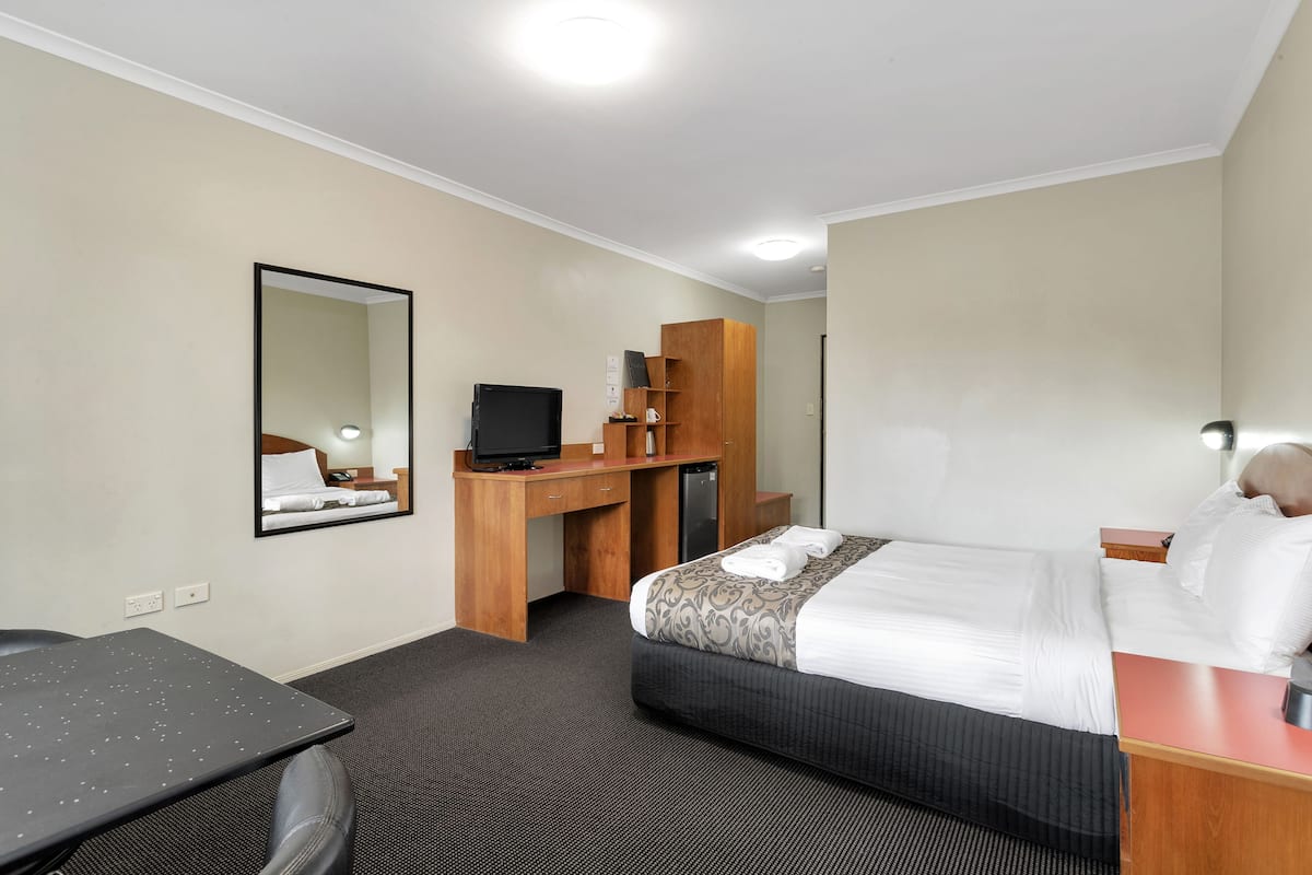 A hotel room with a bed, a desk, a chair, a television, and a mirror.