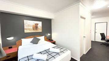 Una camera d'albergo con un letto, un comodino, una lampada, un telefono, una sedia e una porta.